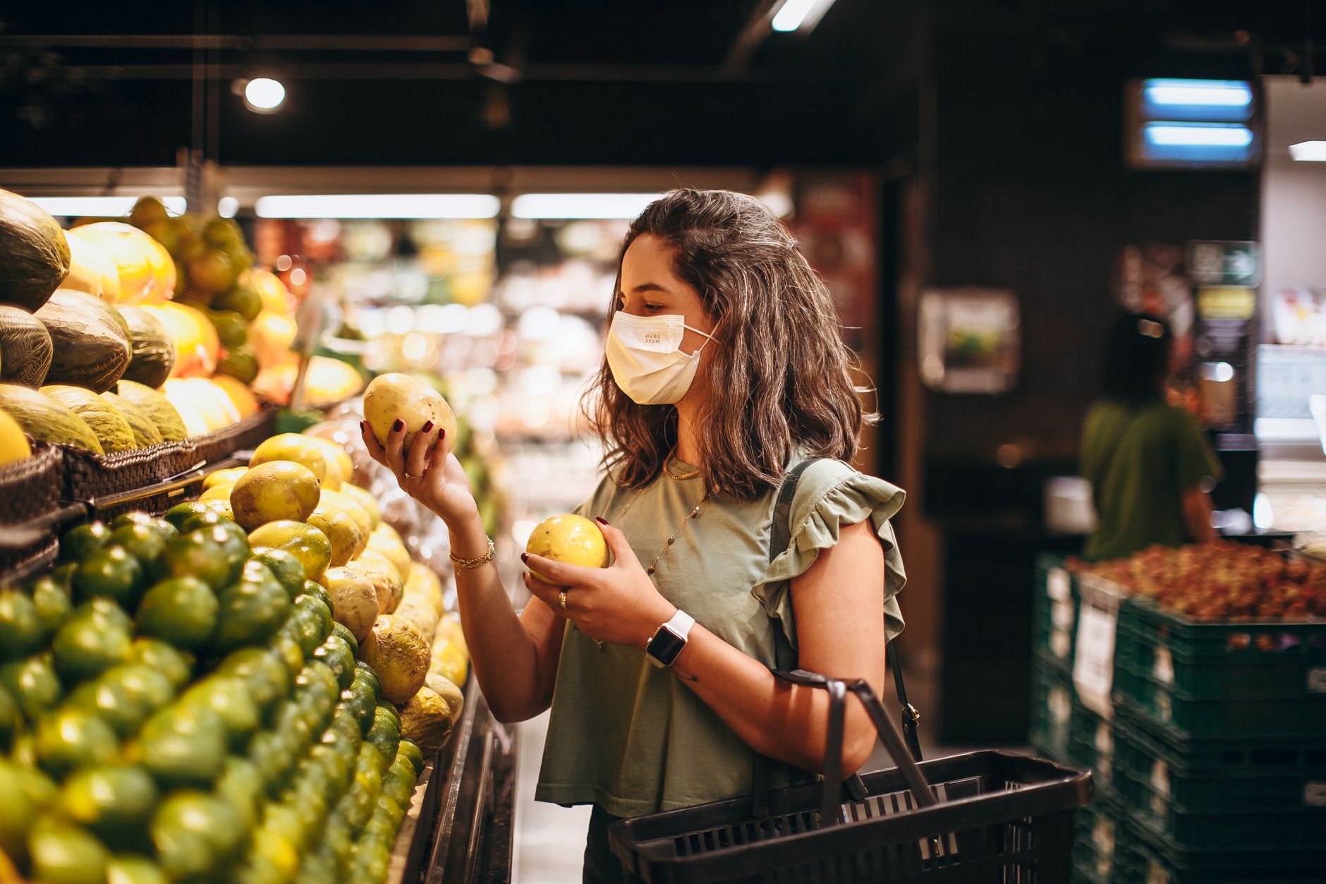 Kobieta w maseczce wybiera świeże owoce w alejce supermarketu