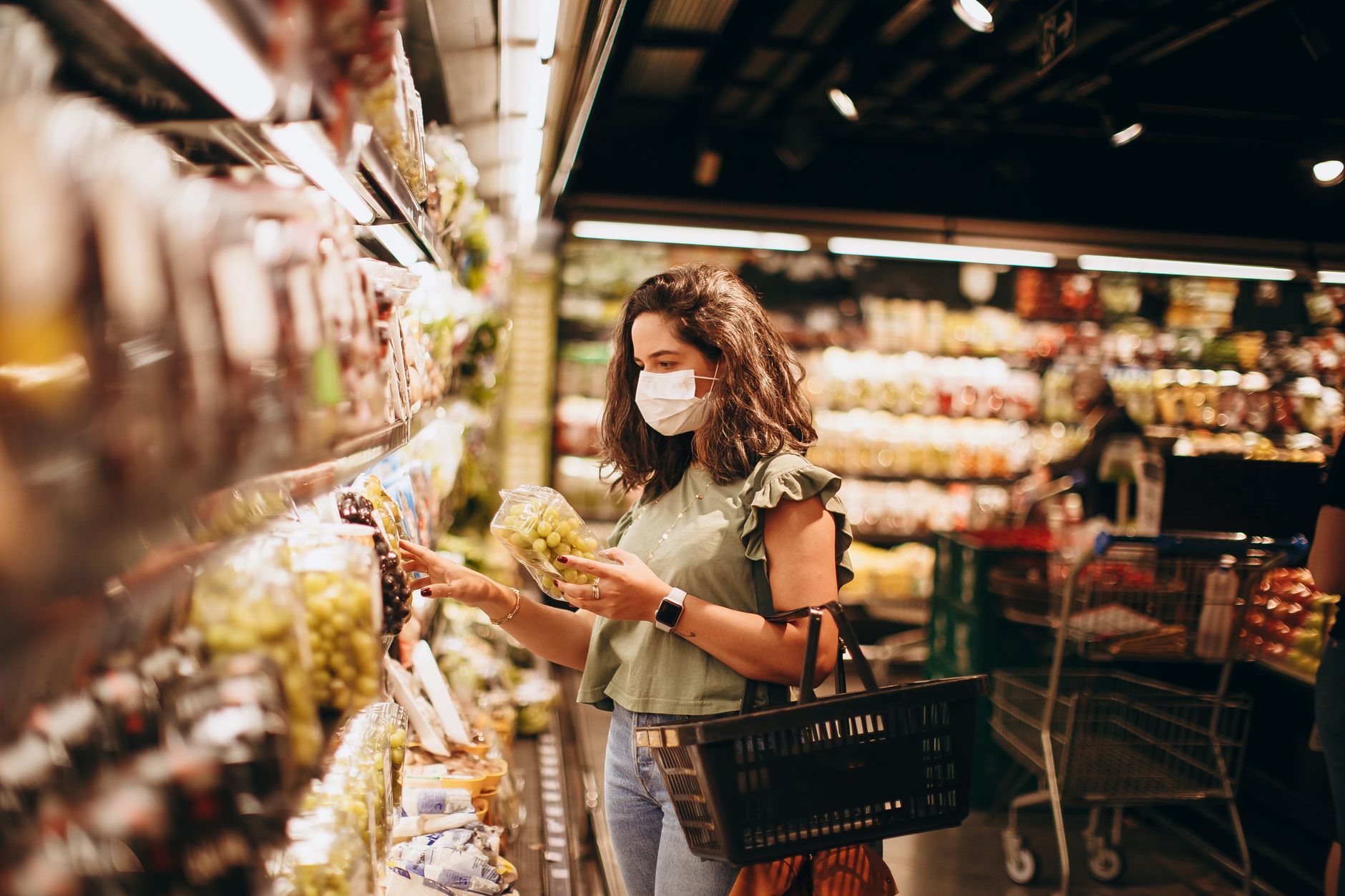 Kobieta w maseczce wybiera winogrona w supermarkecie