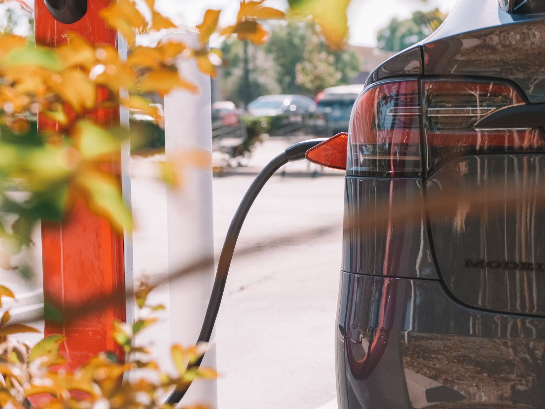 Tesla ładowana przy publicznej stacji na tle zaparkowanych aut